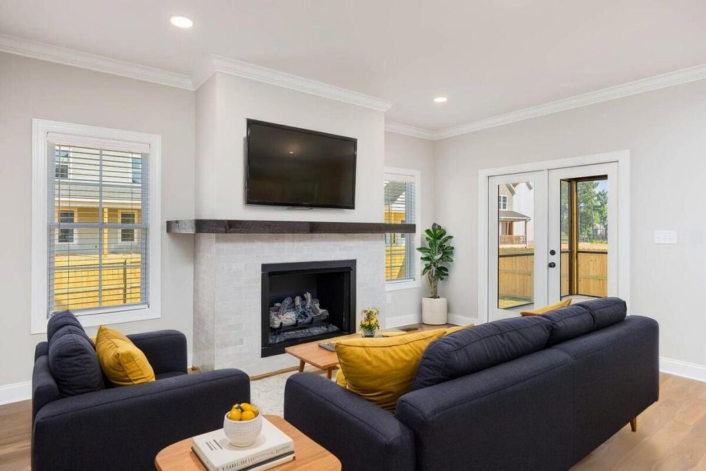 AI-staged living room with navy sofas, yellow pillows, and a fireplace.